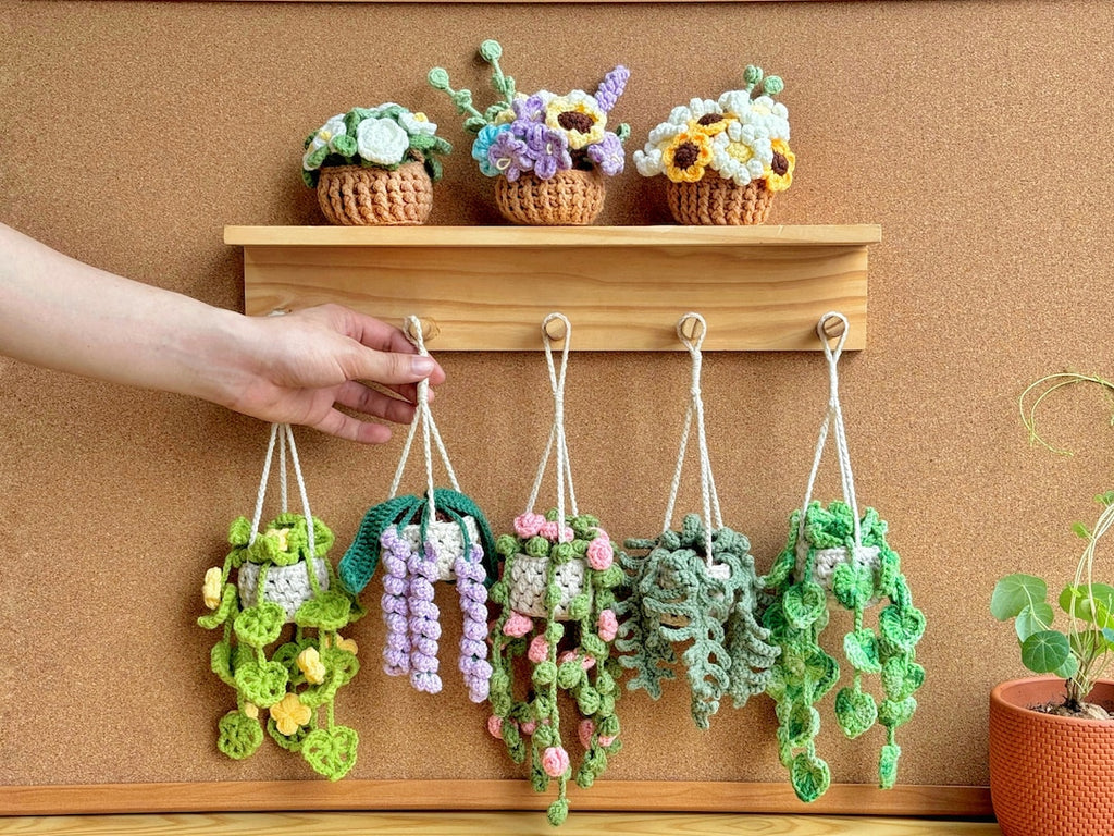Crocheted hanging plant pots with colorful flowers on a wooden shelf